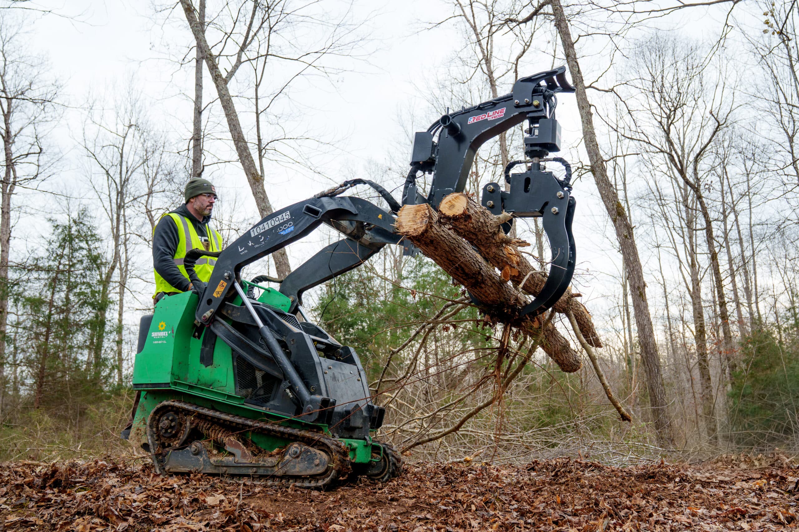 Mini skid steer log grapple carrying a log across a job site