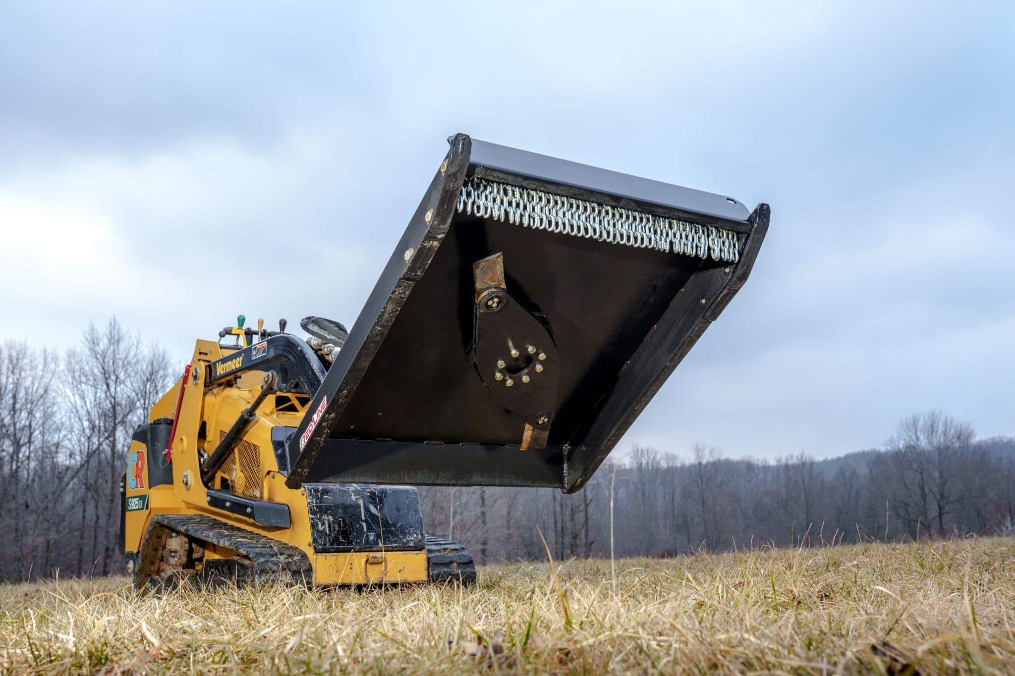 Skid steer running a Red Line brush cutter attachment